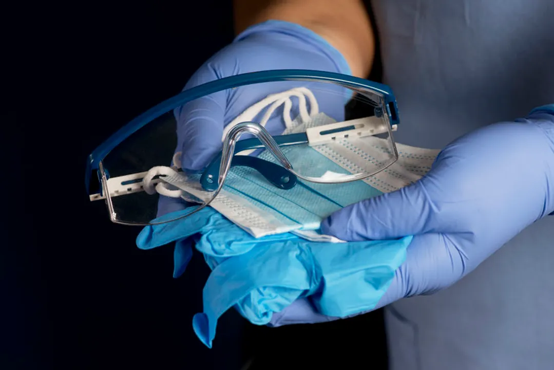 Nurse holding personal protection equipment; gloves, masks, and safety glasses.