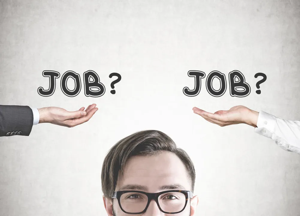 Head of a smart young healthcare provider wearing glasses and smiling. A concrete wall background with two hands offering jobs. A career choice concept